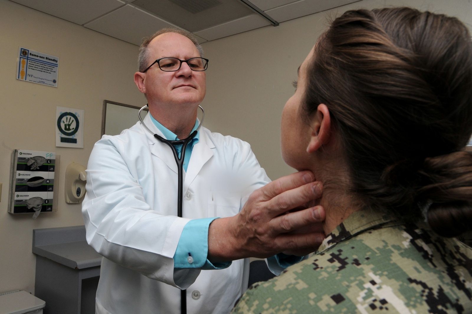 A nurse practitioner in a white coat examines a patient at a Navy family medicine clinic